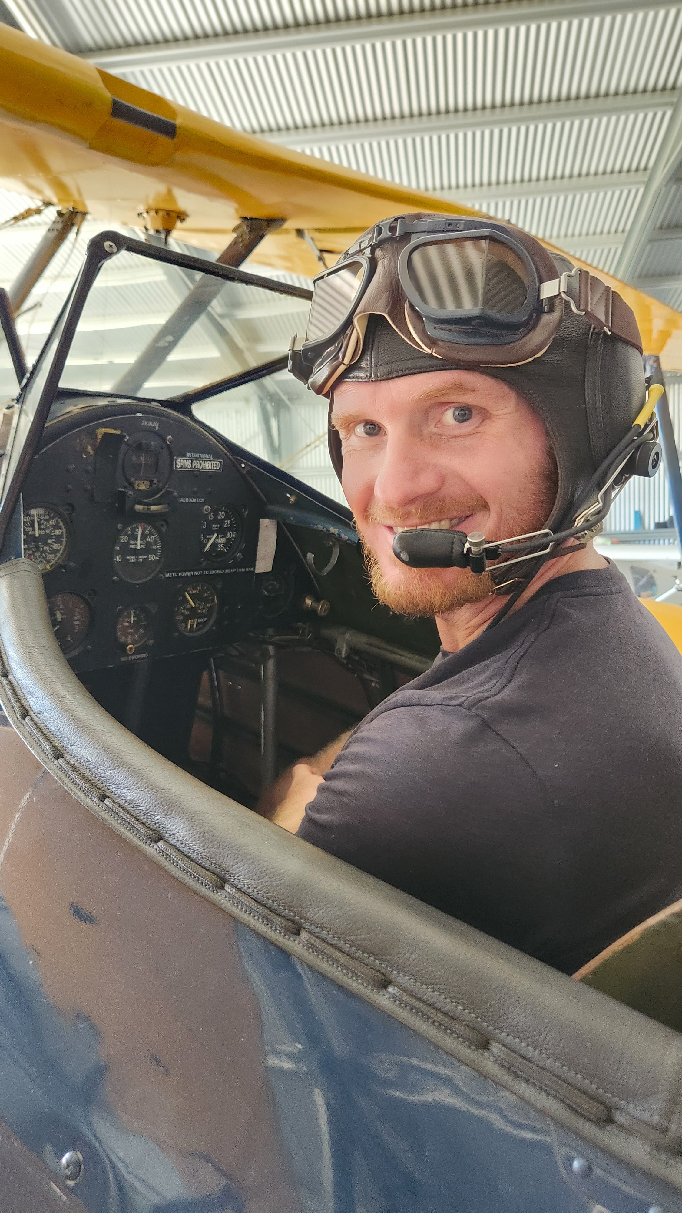 Person inside a Boeing Stearman aircraft cockpit wearing a helmet and goggles.