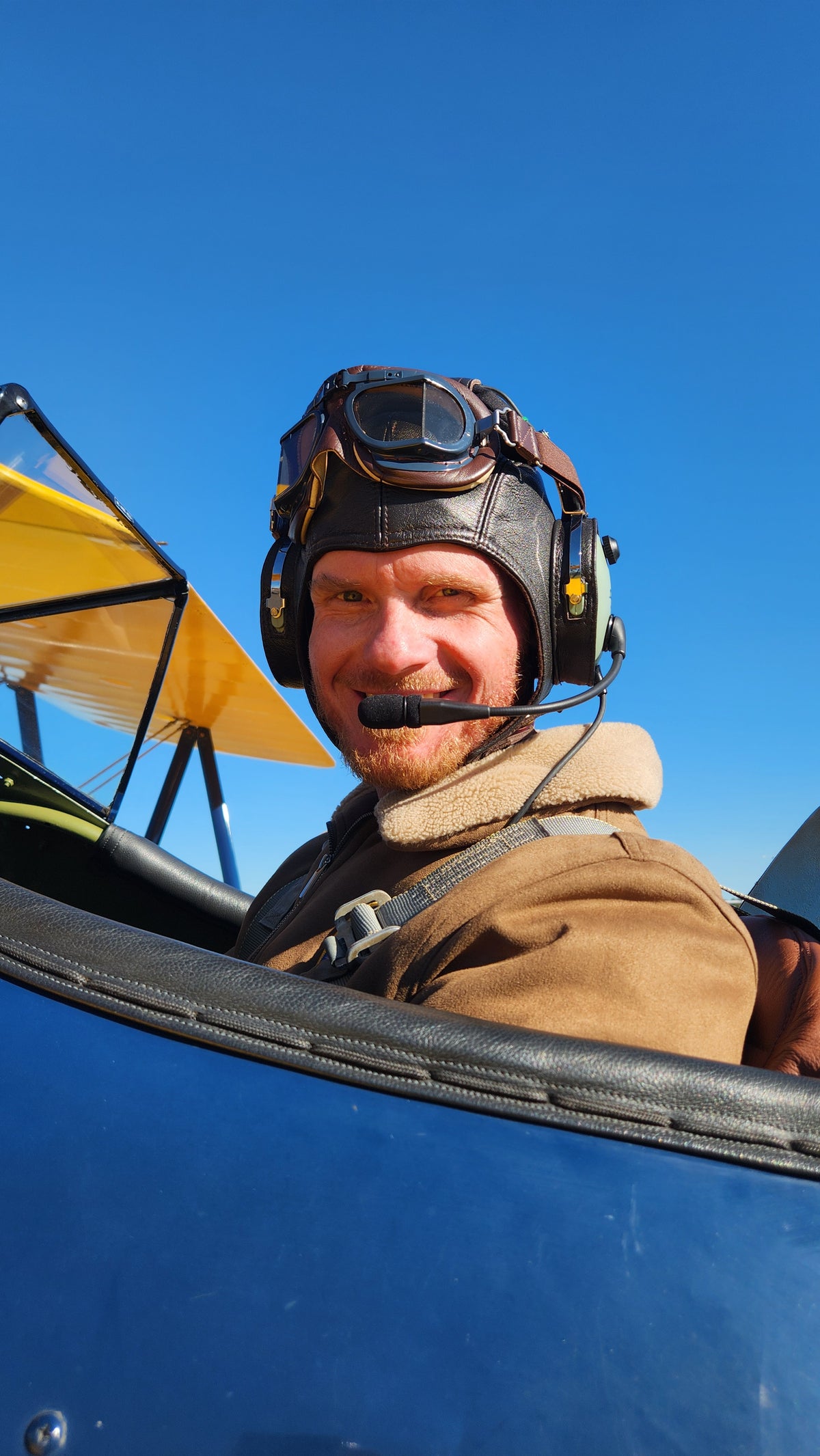 Open Air Adventure Flights pilot Johan Strydom smiling in the cockpit of Winnie, the 1941 Boeing Stearman, wearing a vintage leather flying helmet and goggles.