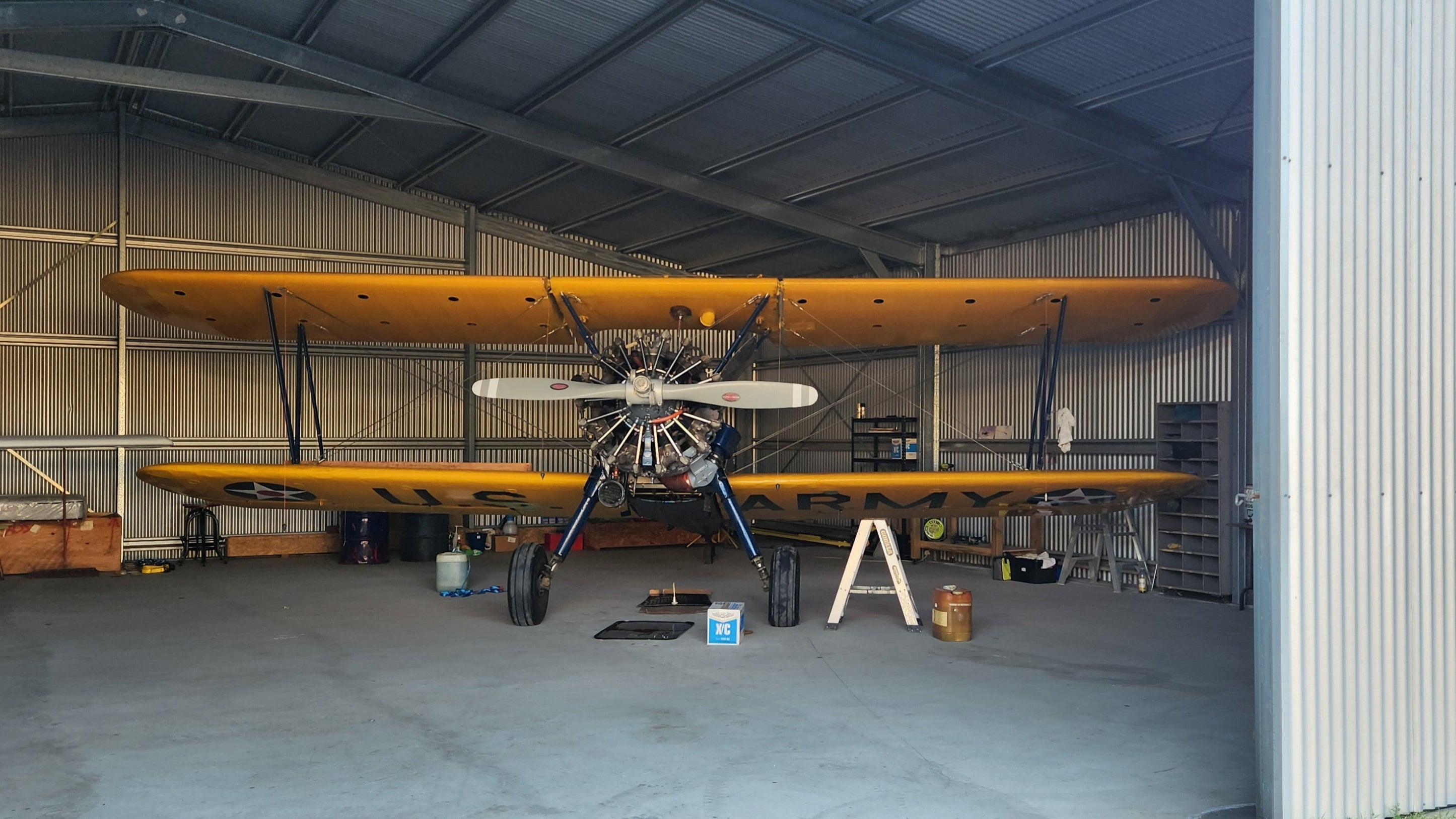 A small airplane inside a hangar with an open door. Boeing Stearman.
