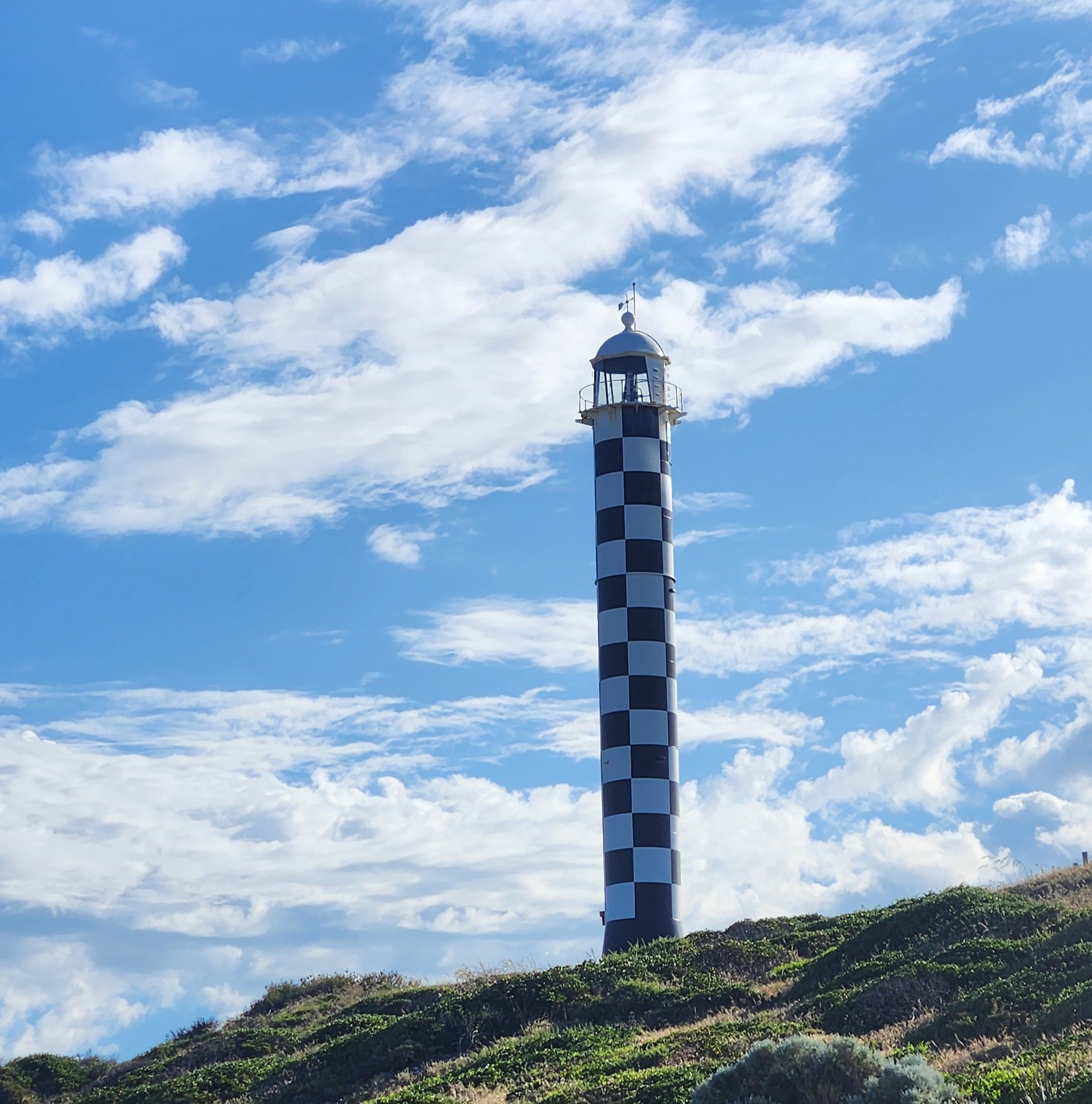 Checkered lighthouse on a grassy hill with a blue sky and clouds, Bunbury WA