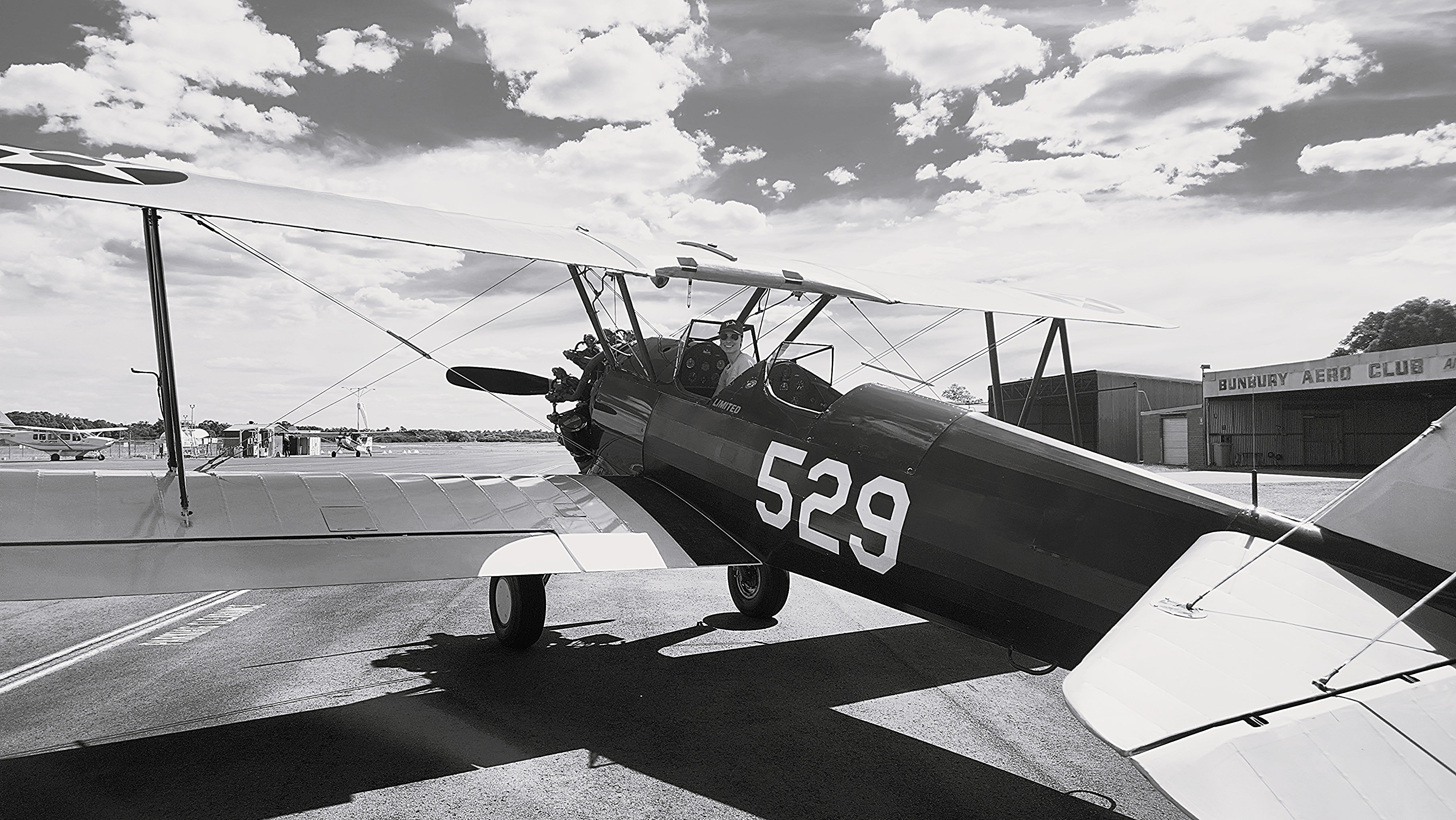Vintage biplane with the number 529 on a runway with a building and trees in the background.