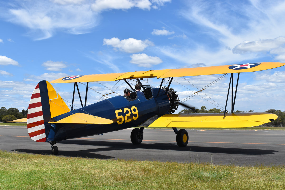 Vintage yellow and blue Boeing-Stearman biplane on runway with cloudy sky.