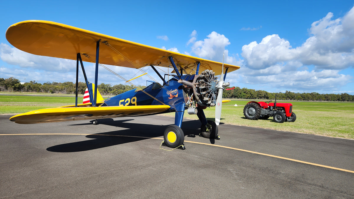 Winnie, the restored 1941 Boeing Stearman, parked on the tarmac beside a tractor at Bunbury Airport.
