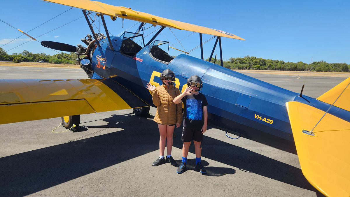 Two children standing in front of Winnie, the 1941 Boeing Stearman, before their Open Air Adventure Flights experience in Bunbury.