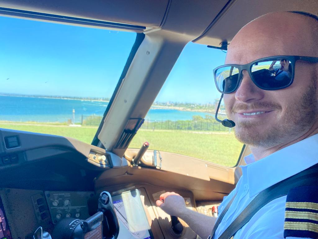 Johan Strydom in the cockpit of an Emirates Boeing 777 with a beach and coastline visible in the background.