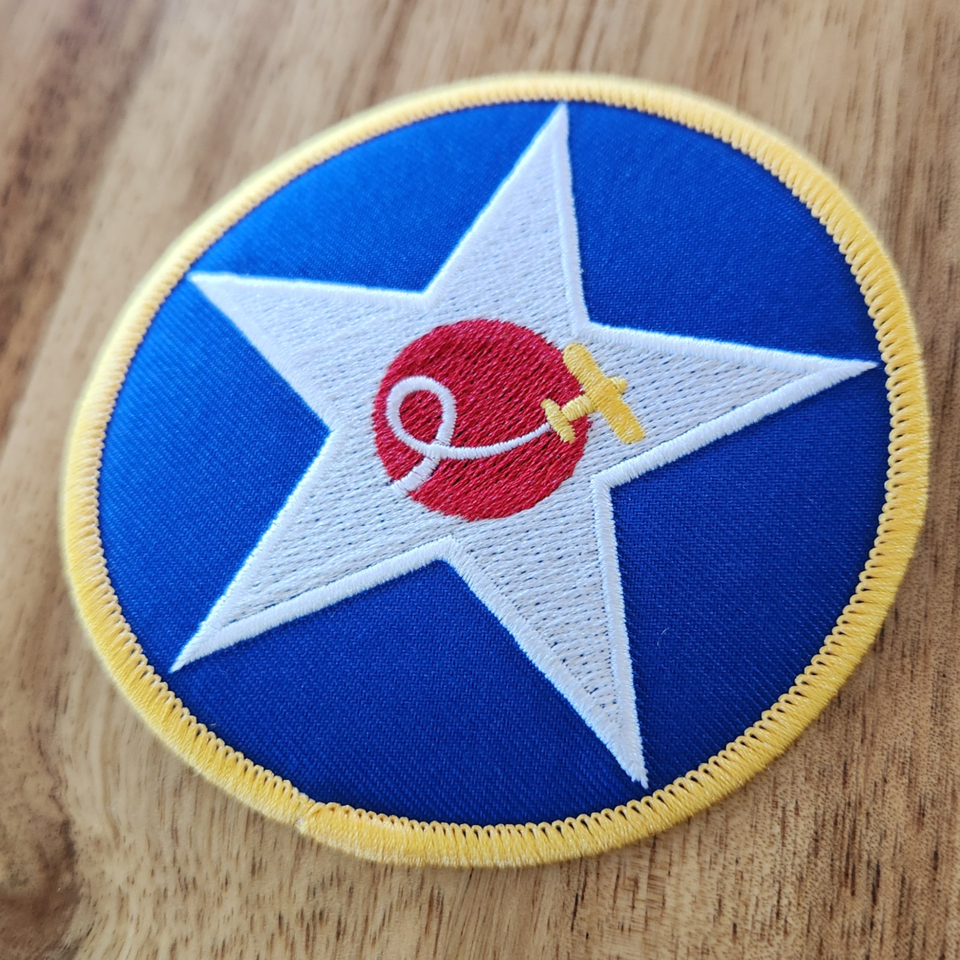 Open Air Adventure Flights embroidered star roundel iron-on patch featuring the aircraft swirl logo, displayed on a wooden table.