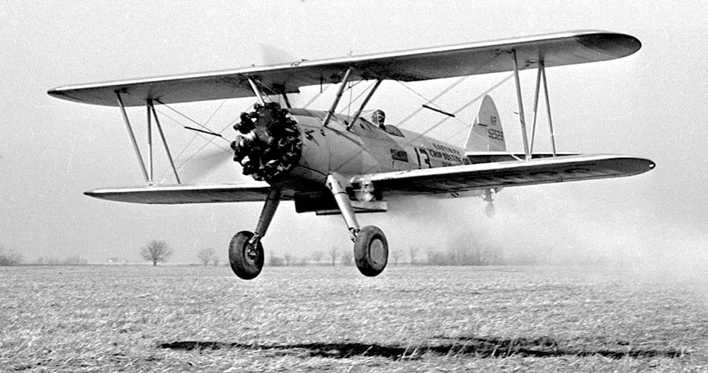 A vintage Boeing-Stearman biplane with an uncowled radial engine flying close to the ground, showcasing a nostalgic open-air aviation experience.