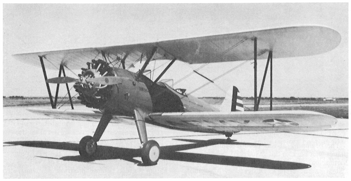 An archival black and white photograph of a Boeing-Stearman Model 75 military trainer biplane parked on an airfield runway. 